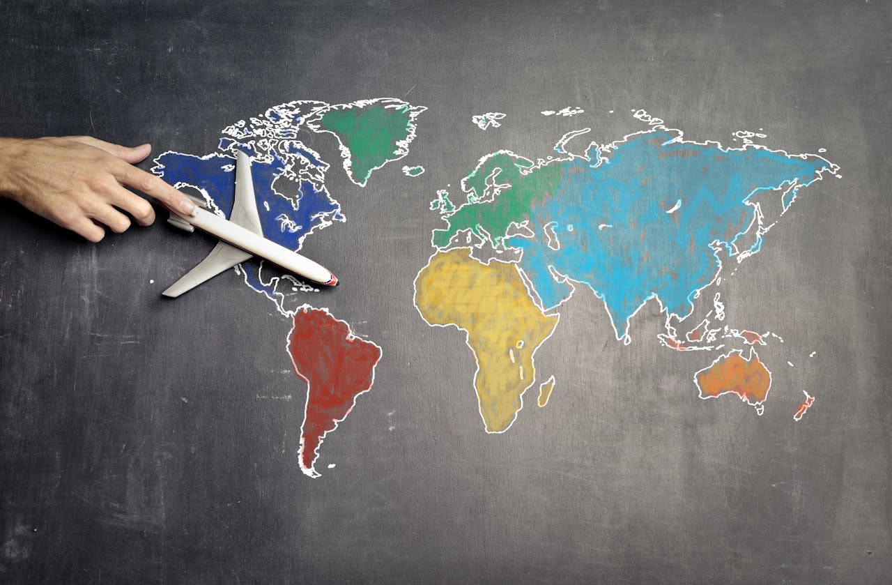 Services Top view of crop anonymous person holding toy airplane on colorful world map drawn on chalkboard