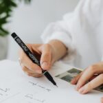 Close-up image of a hand writing with a black pen on paper, focusing on creativity and planning.