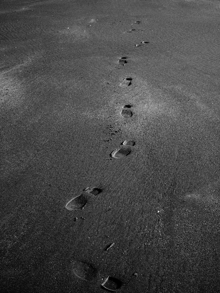 Black and white image of footsteps in sand, capturing a quiet and reflective mood.